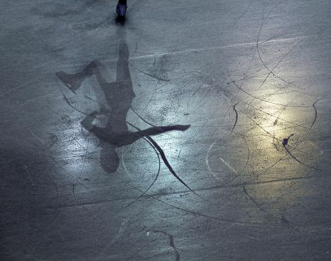 A female skater’s shadow on the surface of the ice.