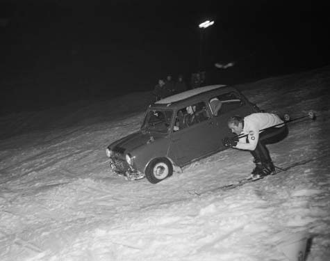 A speed skier and car going down a snowy slope.