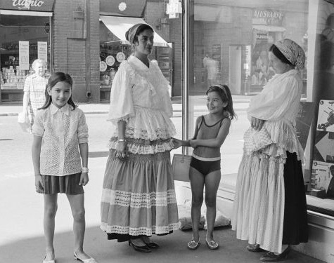 Two women in Roma clothing and two girls in summer clothing in front of a display window.